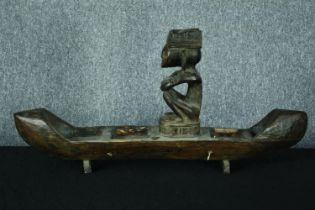 A large carved wooden canoe with a serene looking seated figure. H.39 W.80 cm.