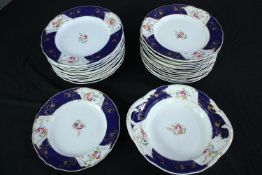 A collection of 26 plates and a serving dish. With scalloped edges and a matching floral pattern.