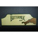 A hand painted sign. 'The Buttermilk Shop'. Decorated with the county of Cornwall. H.61 W.180 cm.