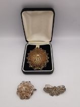 Three white metal filigree wirework brooches, a butterfly, flower and an oval gilded floral design