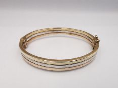 A modern 9ct three colour gold hinged bangle. The bangle comprised of three bands, white, rose and