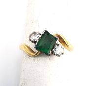 An Edwardian 18ct yellow gold and white metal emerald and diamond cross over ring. Set to centre