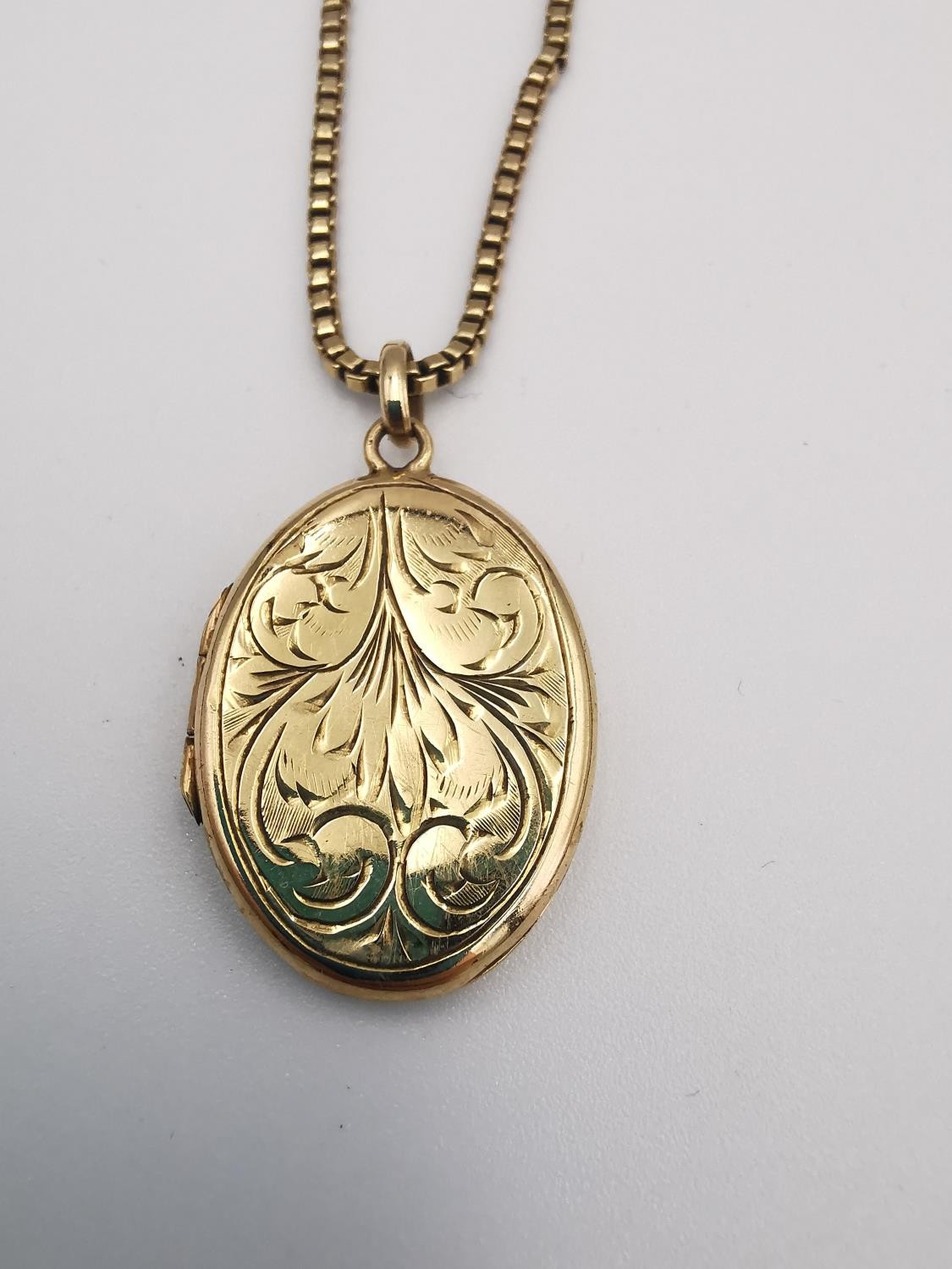 A 9ct yellow box chain and 9ct yellow gold engraved oval locket. The oval locket with a stylised