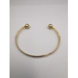 A 9ct yellow gold D-shaped bangle with ball ends. Hallmarked for 9ct. Weight.11.42g Dia.7cm