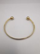A 9ct yellow gold D-shaped bangle with ball ends. Hallmarked for 9ct. Weight.11.42g Dia.7cm
