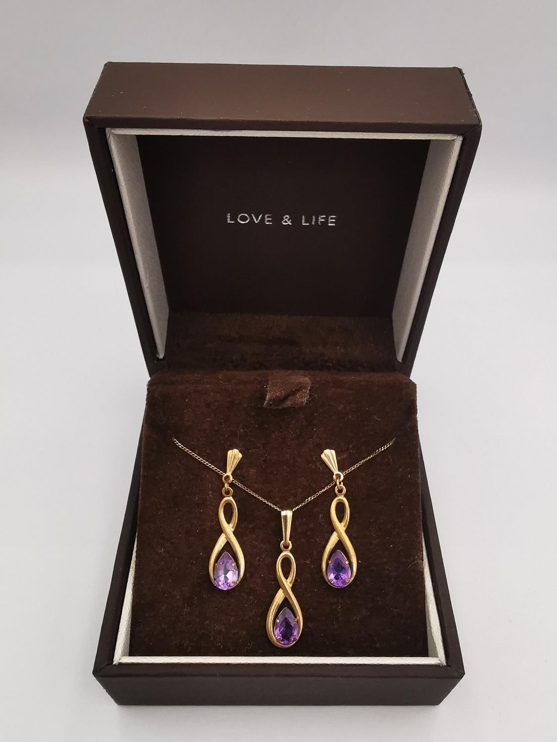 A 9ct rose gold and amethyst pendant with chain and earrings set. The infinity design pendant set