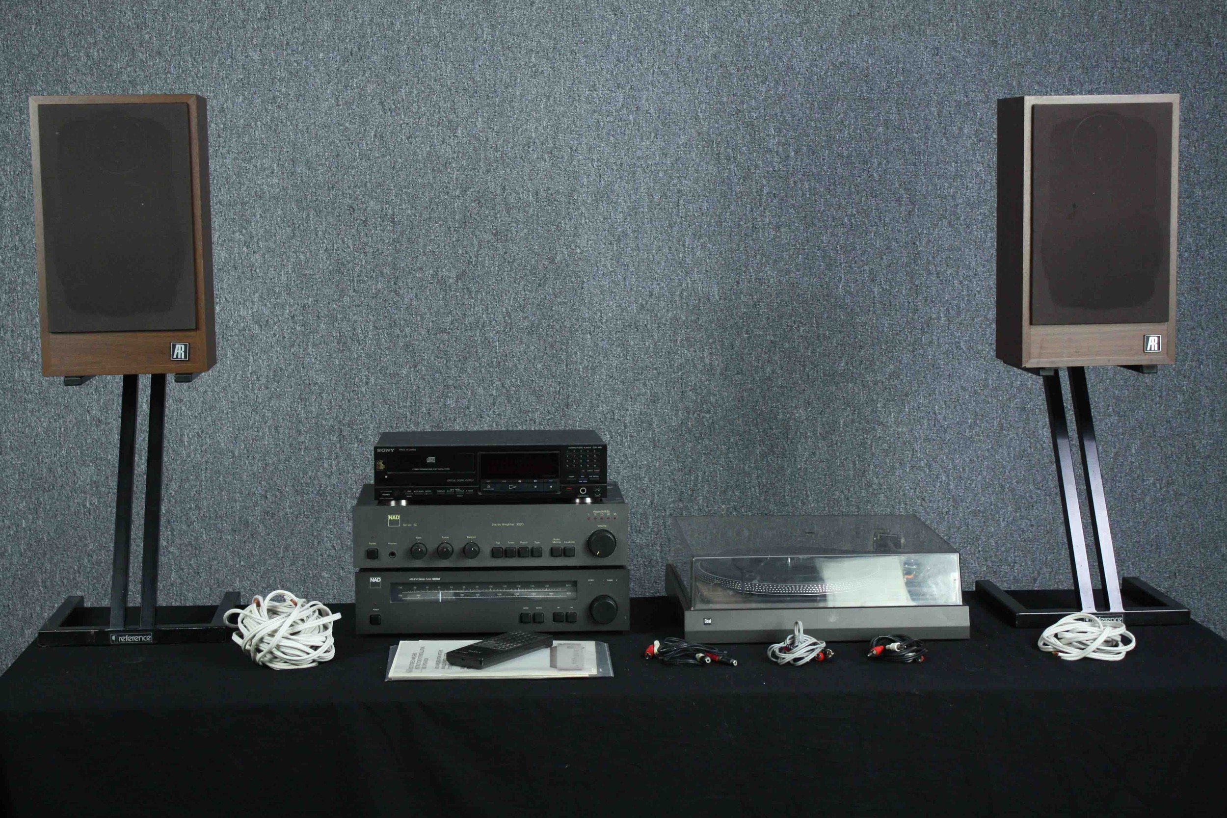 Hi-Fi stack made up of NAD amplifier and tuner. Dual turntable. A&R speakers. The woofer has some