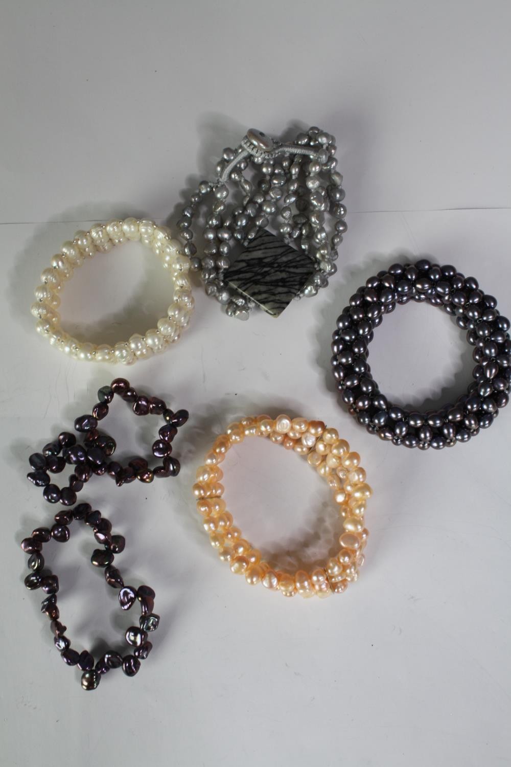 A collection of six cultured pearl elasticated bracelets of various designs, including a grey