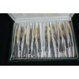 A box of cutlery. Knifes and forks with aluminium handles and gilt decorated finish. Twelve items in