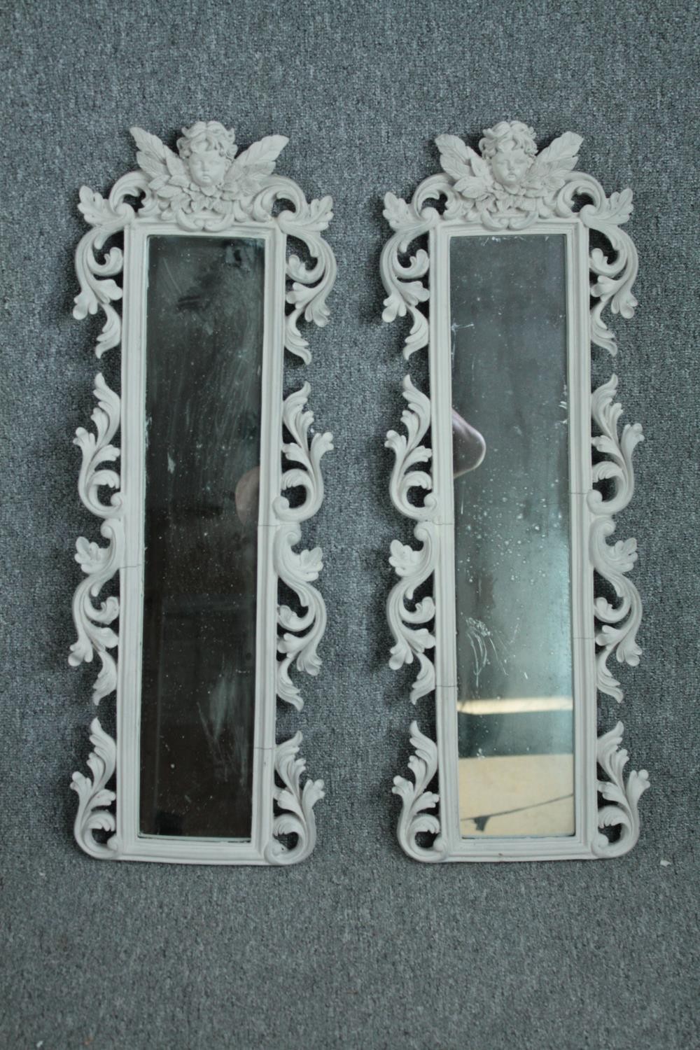 A pair contemporary pier mirrors with floral decorated frames and cherub surmounts. H.80 W.28cm. (