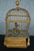 A early 20th century clockwork bird cage housing a feathered song bird. Damaged. H.30 W.17 D.14cm.