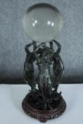 A crystal glass ball supported by three nymphs or maybe the three graces. Metal on a wooden stand.