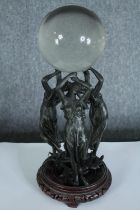 A crystal glass ball supported by three nymphs or maybe the three graces. Metal on a wooden stand.