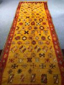 A hand woven Eastern runner with stylised motifs across the ochre field within a deep terracotta