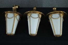 Three brass hanging ceiling lamps with white glass shades. Twentieth century. H.37cm. (each)