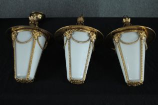 Three brass hanging ceiling lamps with white glass shades. Twentieth century. H.37cm. (each)