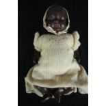 An early 20th century African baby ceramic doll in a knitted yellow woollen dress.H.45cm.