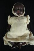 An early 20th century African baby ceramic doll in a knitted yellow woollen dress.H.45cm.