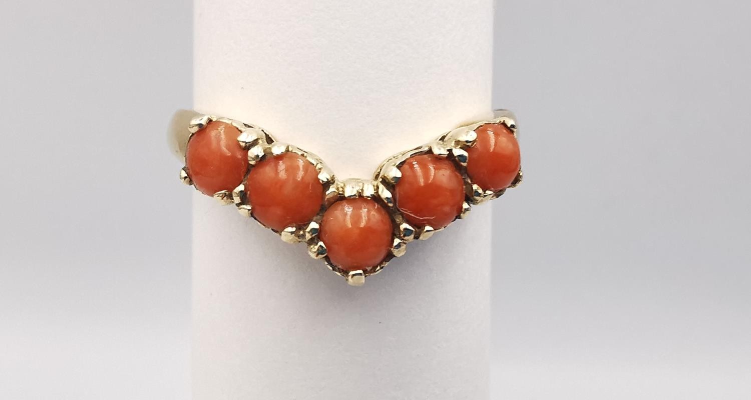 A 9ct yellow gold coral V-shaped ring. Set with five round red coral cabochons in open back claw