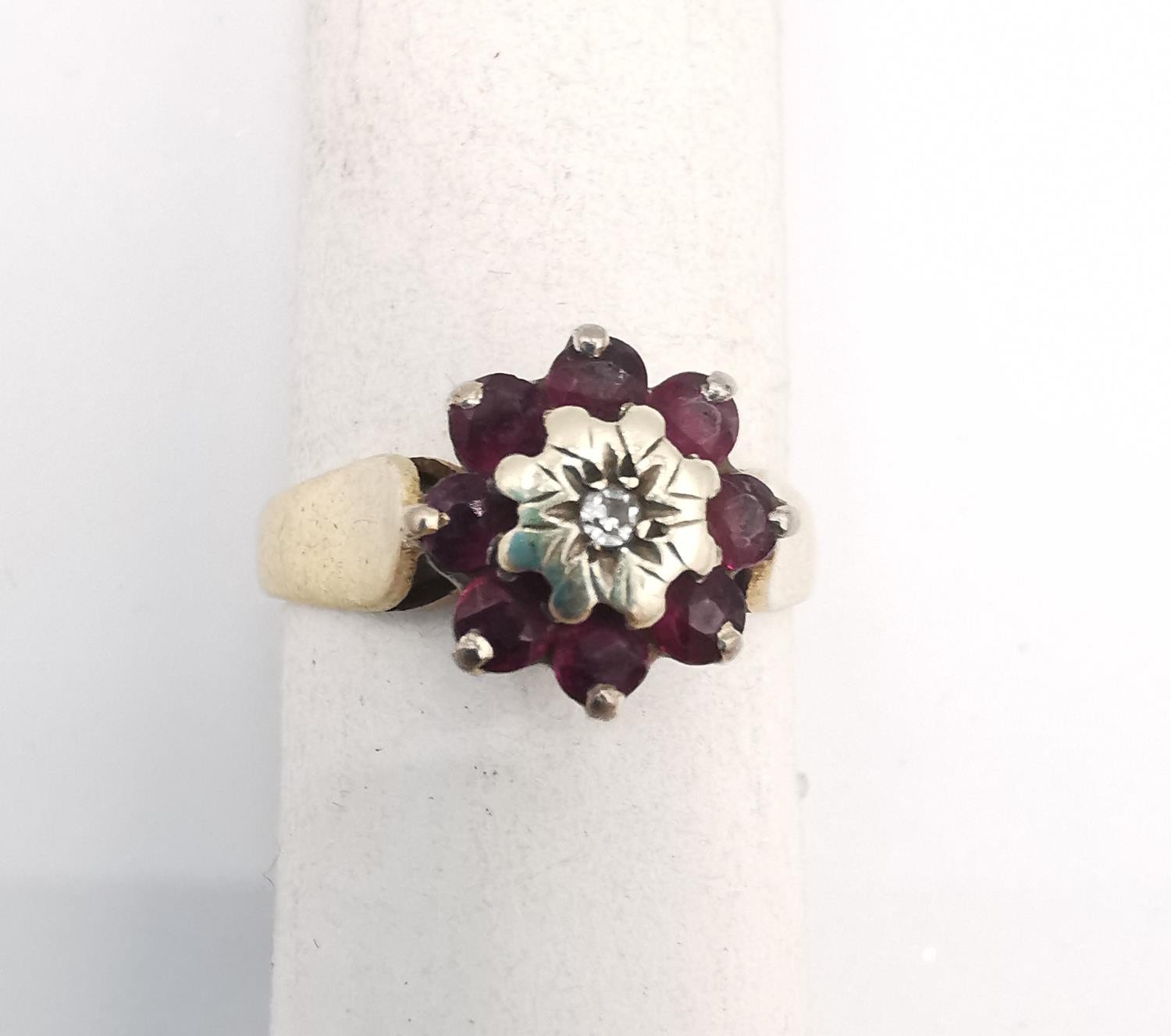 A pink metal (tests as 9ct) ruby and diamond cluster ring. Ring set to centre with a round eight cut