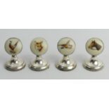 A set of four George V silver weighted menu holders with hand painted/enamelled inset plaques,