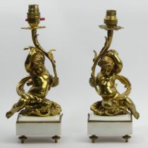 A pair of polished bronze cherub lamps on white marble bases, 30cm x 32cm. UK Postage £20.