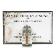 AN EXPLODING SHOTGUN CARTRIDGE TOGETHER WITH A PURDEY & SONS ENAMEL SIGN