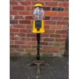 A VINTAGE AMERICAN GUMBALL MACHINE ON CAST IRON BASE, with yellow painted alloy body and glass