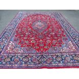 A LARGE CARPET WITH RED CENTRAL GROUND AND BLUE BORDER, APPROX 360 X 270 CM - WEAR THROUGHOUT