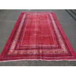 A LARGE RED GROUND WOOLLEN CARPET WITH PATTERNED BORDER APPROX 320 X 210 CM