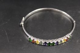 A WHITE METAL BANGLE STAMPED 500 SET WITH AN ASSORTMENT OF MULTI-COLOURED STONES
