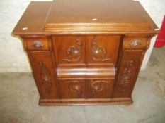 A CARVED MAHOGANY SEWING MACHINE CUPBOARD WITH A MODERN SEWING MACHINE FITTED