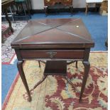 AN EDWARDIAN MAHOGANY ENVELOPE GAMES TABLE, the leaves opening to a baize lined interior, with