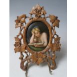 A 19TH CENTURY CONTINENTAL OVAL PORCELAIN PLAQUE OF A LADY READING, unsigned in a carved wooden