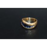 A HALLMARKED 18 CARAT GOLD SWIRL CHANNEL SET SAPPHIRE RING, set with 9 oval and circular