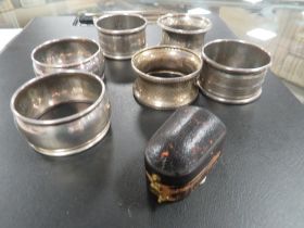 SIX ASSORTED HALLMARKED SILVER NAPKIN RINGS TOGETHER WITH A CASE THIMBLE