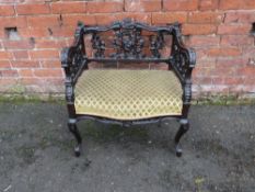 AN EDWARDIAN EBONISED CARVED LOW ARMCHAIR, with an upholstered seat, raised on cabriole supports,