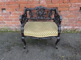 AN EDWARDIAN EBONISED CARVED LOW ARMCHAIR, with an upholstered seat, raised on cabriole supports,