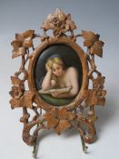 A 19TH CENTURY CONTINENTAL OVAL PORCELAIN PLAQUE OF A LADY READING, unsigned in a carved wooden