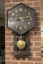 AN UNUSUAL ARTS AND CRAFTS STYLE WALLCLOCK, the hexagonal face with brass numerals, pendulum, H 81