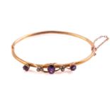 An Edwardian 9ct yellow gold bangle, mounted with an oval mixed cut amethyst flanked by three seed