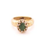 A yellow metal, diamond, and emerald cluster ring, set with a mixed oval-cut emerald, within a