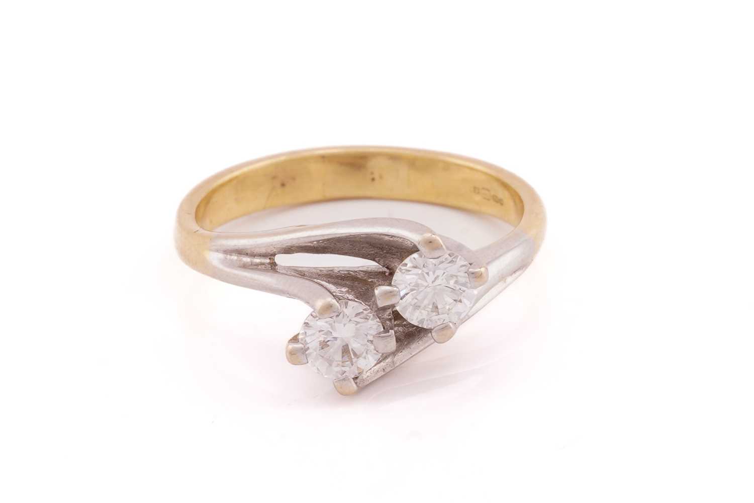 A two stone diamond crossover ring; the round brilliant cut diamonds in four claw mounts to bi-