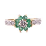 An emerald and diamond cluster ring; the seven stone cluster with central round brilliant cut