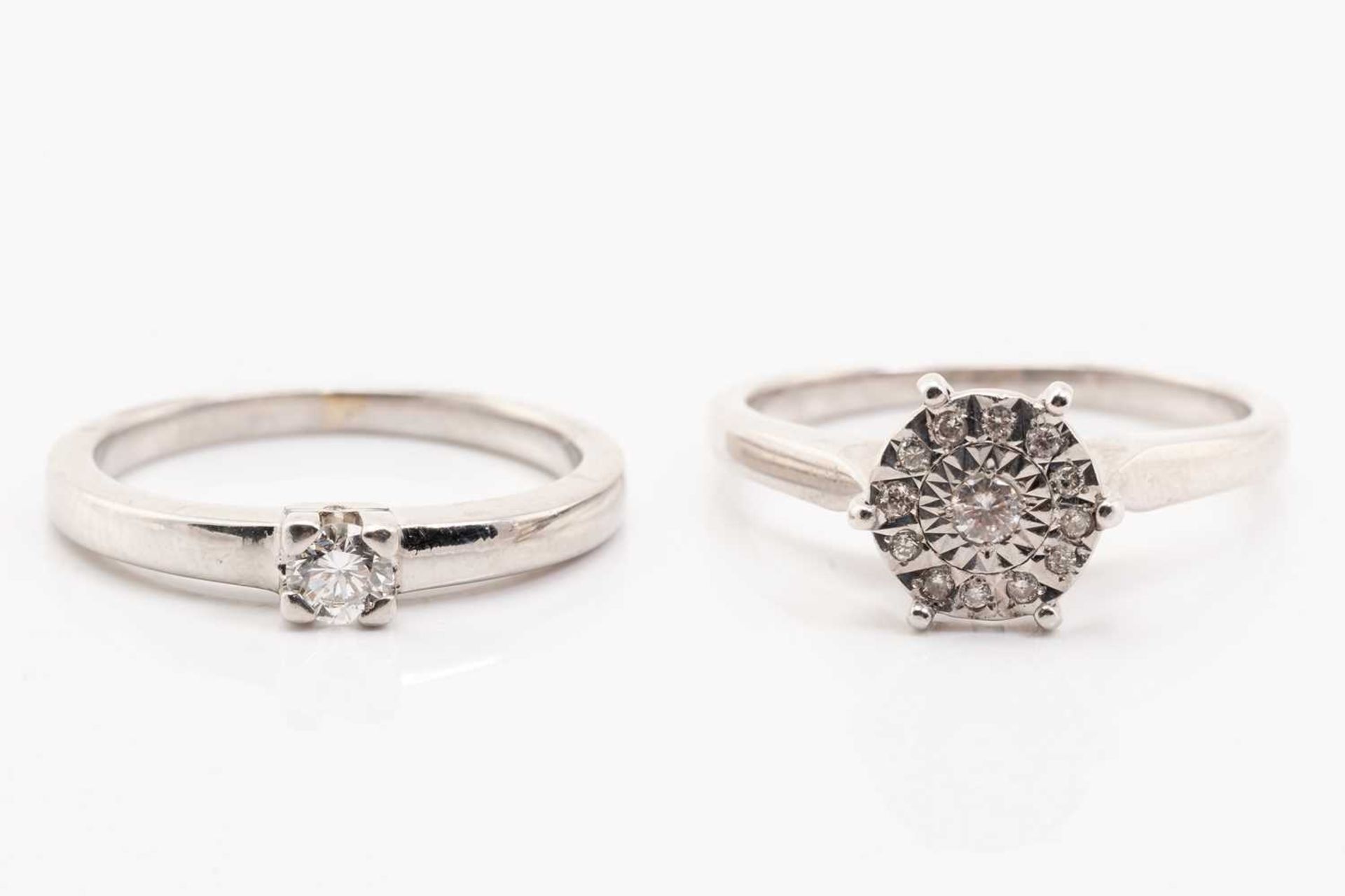 A single stone diamond ring and a diamond cluster ring, featuring a claw set round brilliant cut