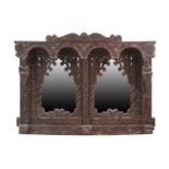 An Indian rustic carved teakwood over mantle mirror with overhanging arcaded cornice above a pair of