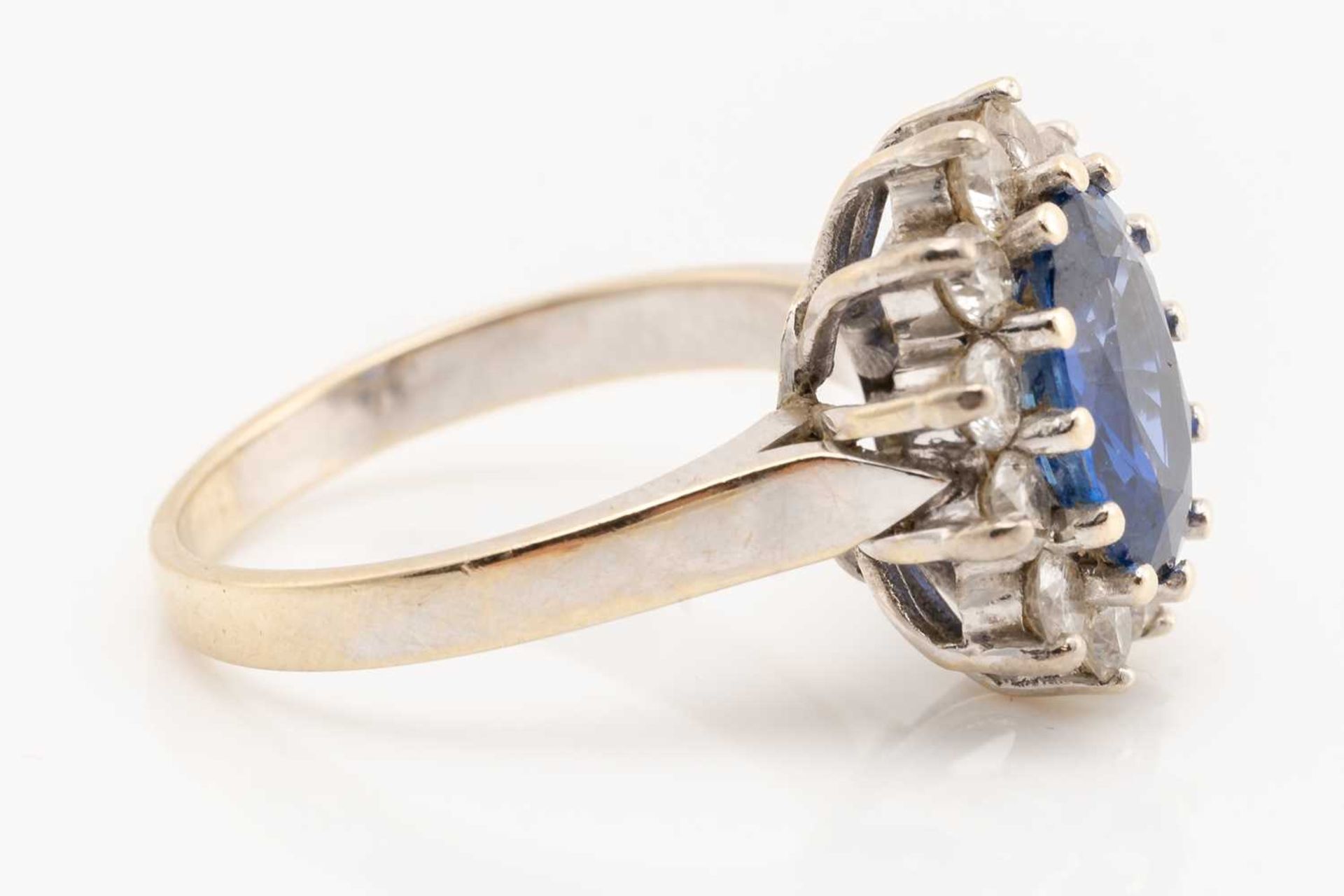 A sapphire and diamond cluster ring; the oval cut sapphire in claw mount above a border of twelve - Image 3 of 6