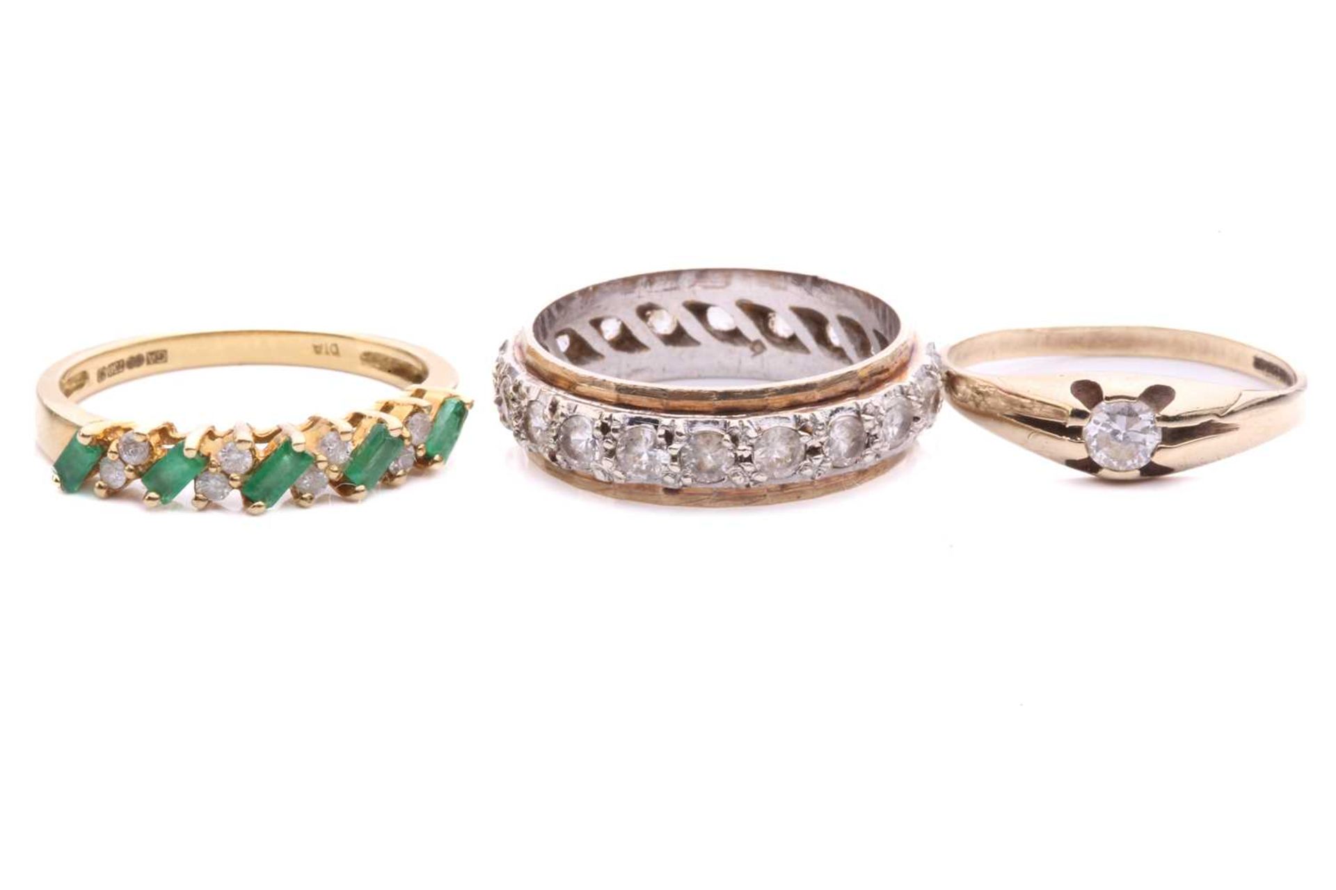 Three gem-set rings in gold; to include an 18ct gold ring set with alternating emeralds and