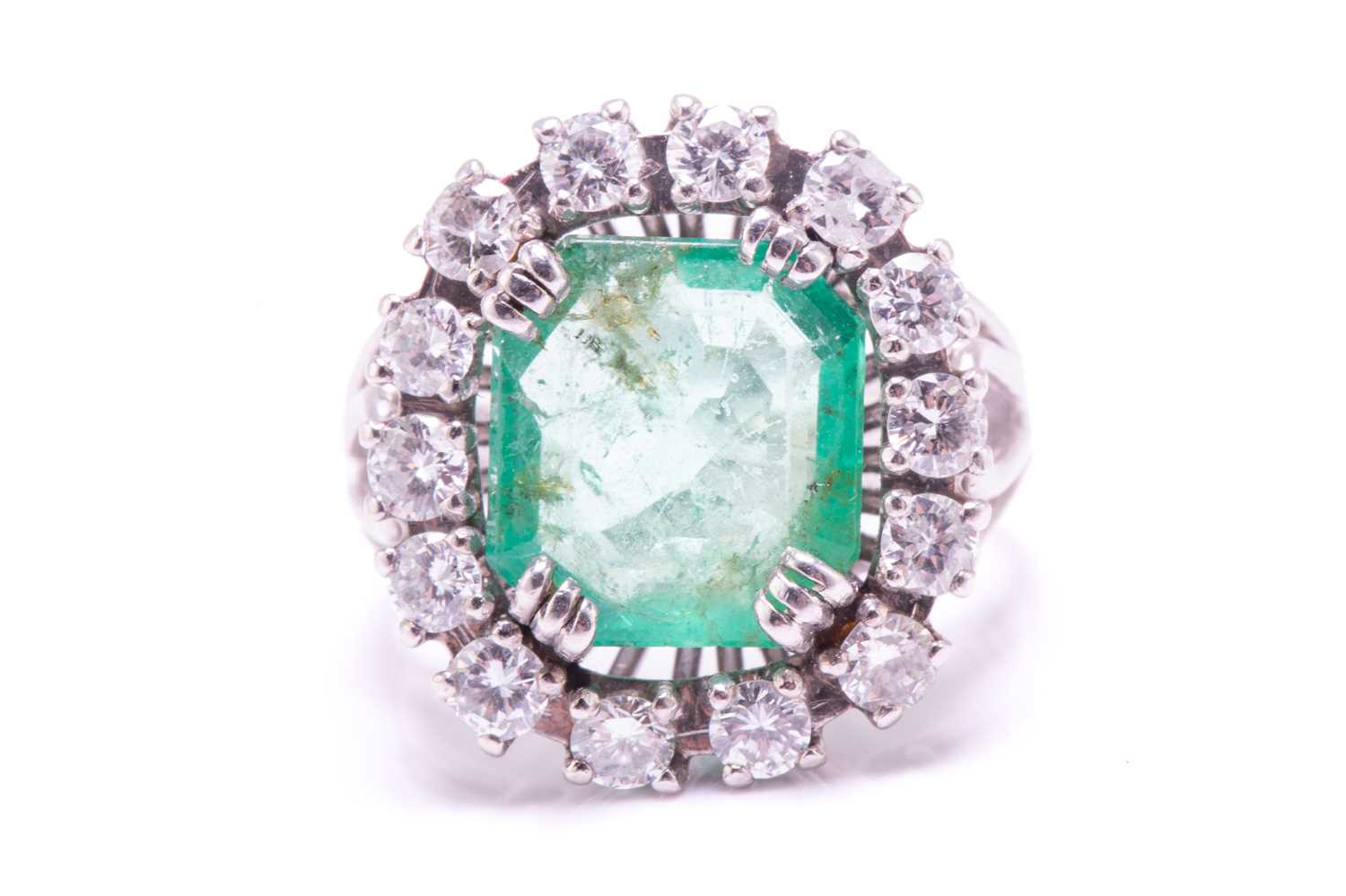 An emerald and diamond entourage ring, centred with an emerald-cut emerald of pale bright bluish- - Image 7 of 12