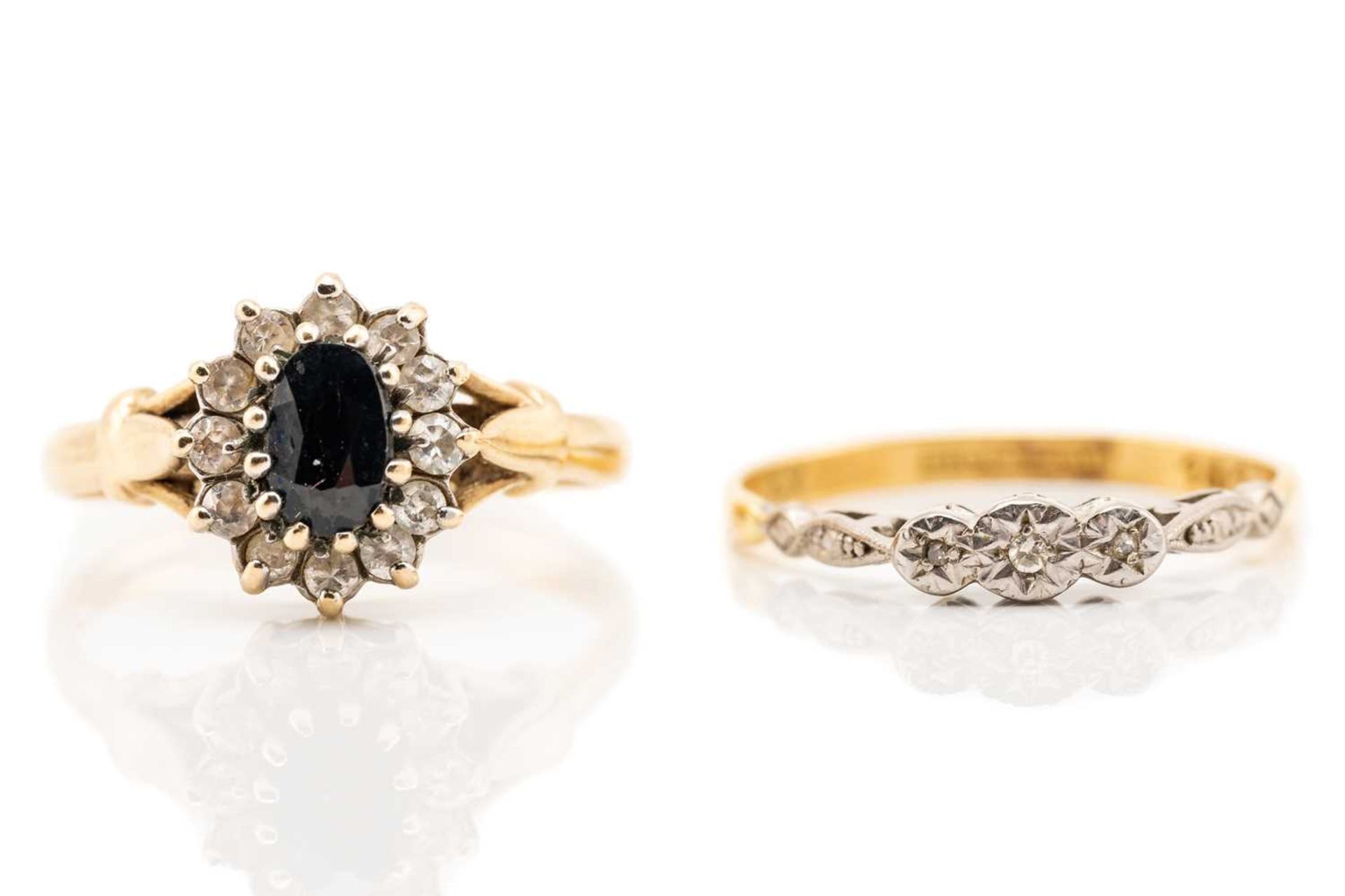 A sapphire cluster ring, the oval cut sapphire in claw mount above a border of twelve clear